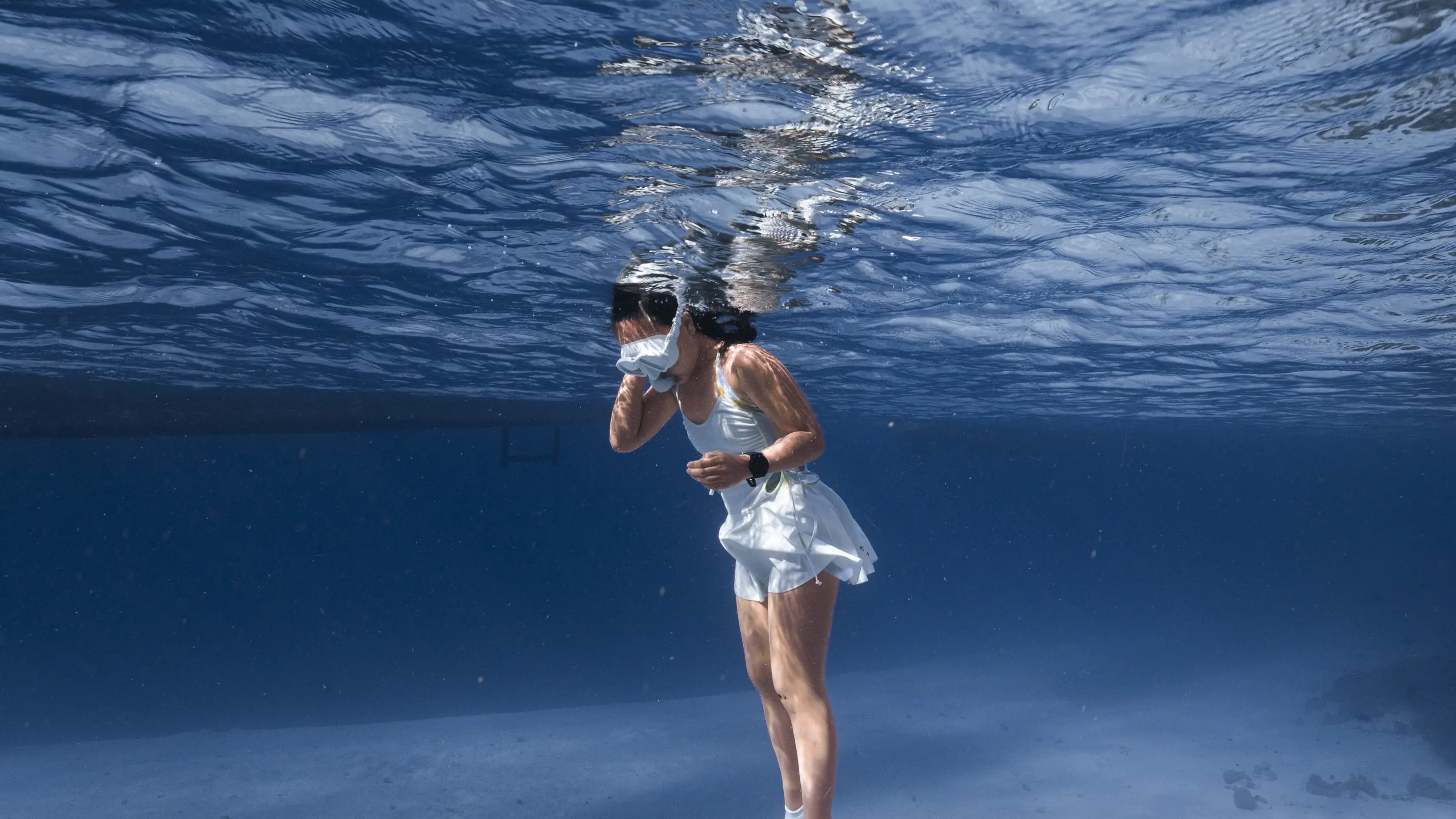 Split-shot di gua laut: freediver dengan fin ungu di bawah permukaan, langit-langit gua di atas air